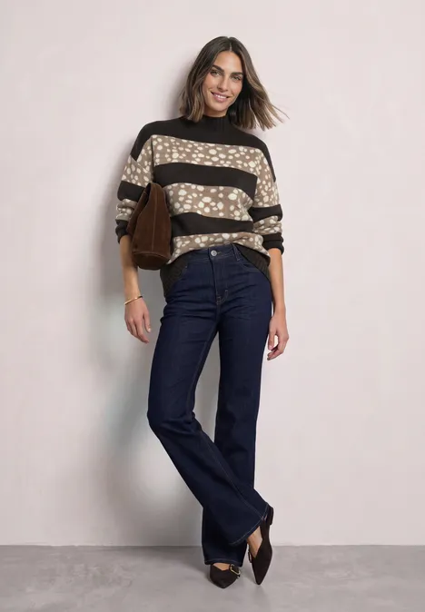 Jacquard Pullover mit Turtle Neck black coffee mel. Frau in gepunktetem & gestreiftem Pullover, dunklen Jeans, spitzen Schuhen und brauner Tasche vor hellem Hintergrund.