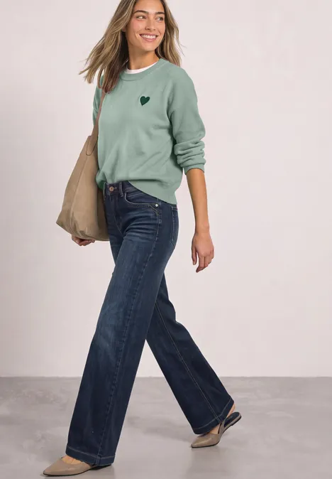 Loose Fit Sweatshirt mit Patch Detail eucalyptus green Eine Frau in weitem Jeans, grünem Pullover und Tasche geht lächelnd.