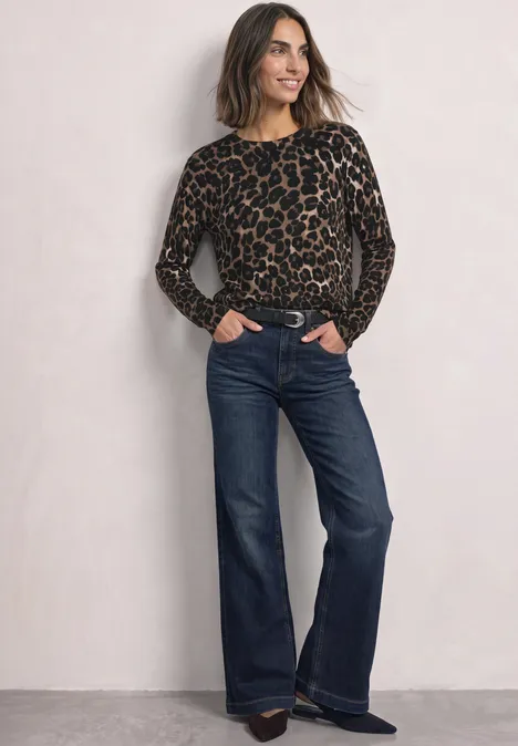 Langarm Pullover mit Rundhals und Leo-Muster Black Frau in Leopard-Pulli und dunkelblauen, weiten Jeans, lächelt mit Händen in den Taschen vor neutralem Hintergrund.