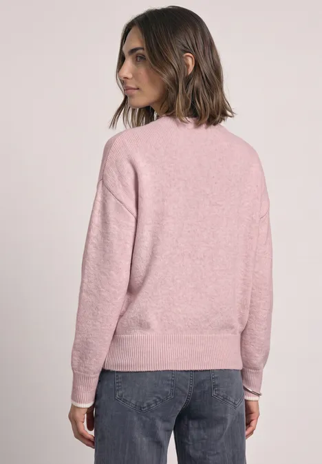 Pull uni à col rond quiet rose mel. Frau von hinten in rosafarbenem Pullover und dunkler Jeans