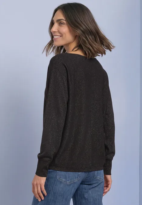 Frau im schwarzen Pullover und Jeans, sieht lächelnd zurück.