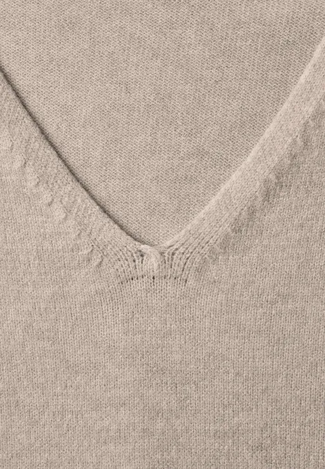 Nahaufnahme eines beigen V-Ausschnitt-Strickpullovers mit feiner Struktur.
