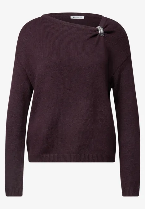Violetter Pullover mit langen Ärmeln, Knotendetail und silberner Brosche an der Schulter.