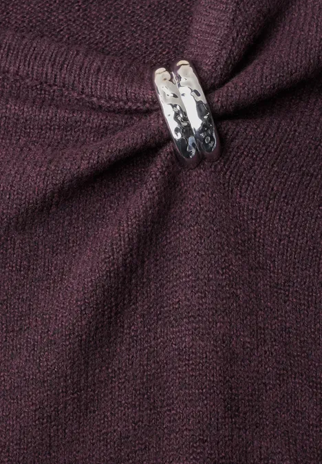 Nahaufnahme eines dunkelroten Strickpullovers mit silbernem Zierrahmen, der den Stoff zusammenhält.