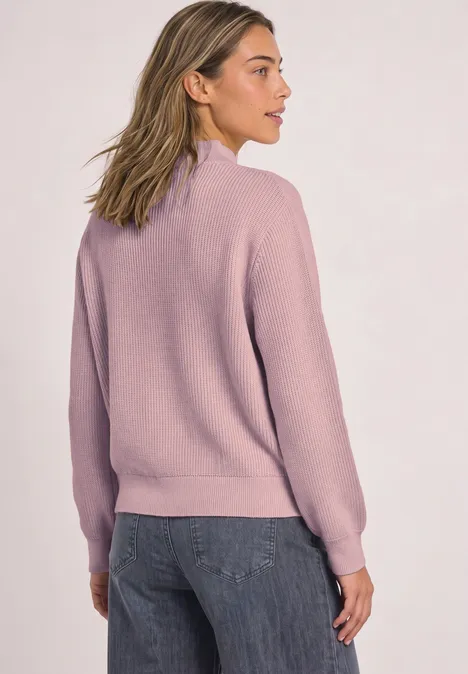 Eine Frau von hinten in einem fliederfarbenen Pullover und Jeans.