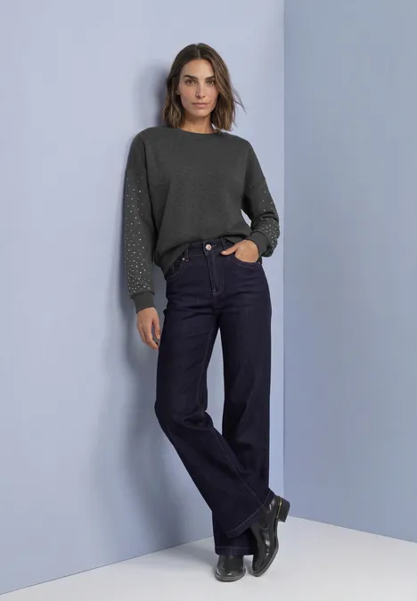 Sweat-shirt ample avec des rivets armor grey mel. Modell mit dunkelgrünem Pullover, weiten Jeans und schwarzen Boots vor schlichtem hellblauem Hintergrund.