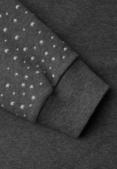 Sweat-shirt ample avec des rivets armor grey mel. Nahaufnahme eines grauen Kleidungsstücks mit runden Noppen auf dem Ärmel und einem Bündchen.