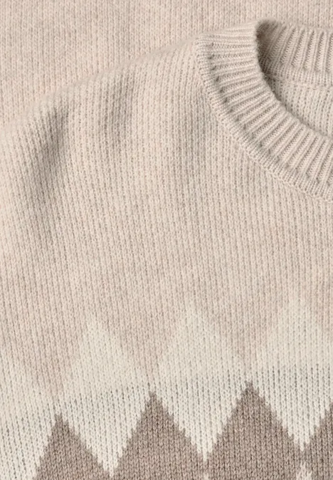Nahaufnahme eines gestrickten Pullovers mit Rautenmuster in Beige und Weiß.
