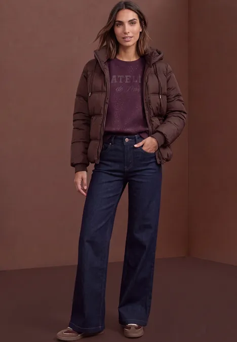 Loose Fit Sweatshirt mit Glitzer berry plum Eine Frau steht vor braunem Hintergrund und trägt eine dunkelbraune Daunenjacke, weite Jeans und Pullover.