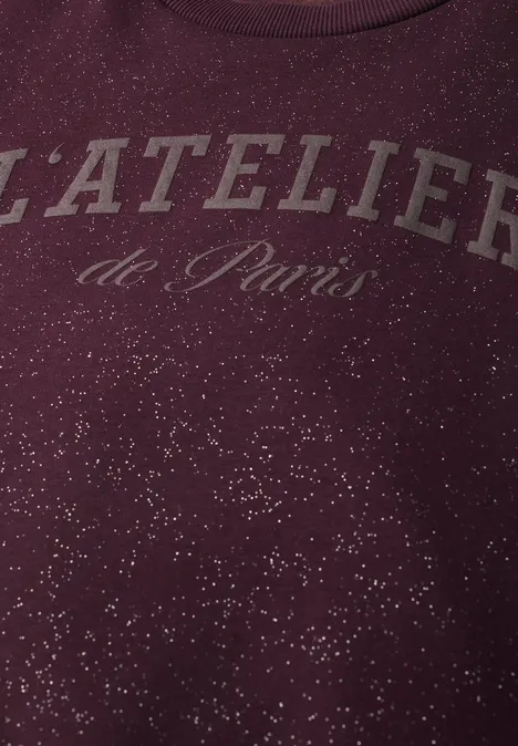 Loose Fit Sweatshirt mit Glitzer berry plum Nahaufnahme eines bordeauxroten Pullovers mit Schriftzug 'L'ATELIER de Paris' und weißen Sprenkeln.