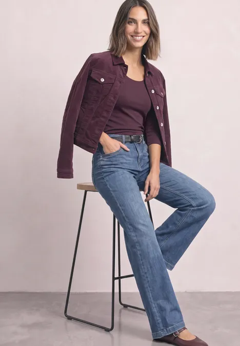 Une femme appuyée sur un tabouret porte un blazer violet, un top assorti et un jean bleu.