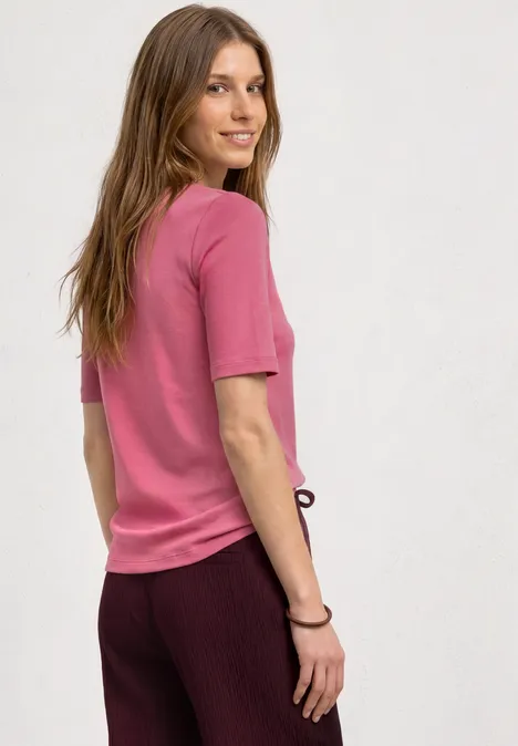 Basic T-Shirt mit V-Neck in Unifarbe blush berry Eine Person in rosa T-Shirt und bordeauxfarbener Hose, seitlich stehend vor heller Wand.
