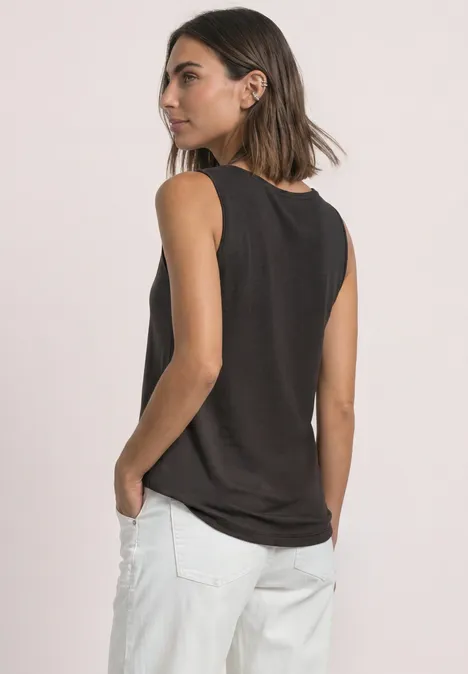Zijdelingse opname van een vrouw in een zwart mouwloos topje en witte broek