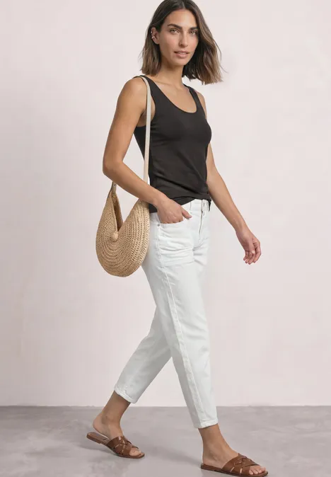Vrouw in zwart hemdje en witte broek, bruine sandalen en rieten tas.