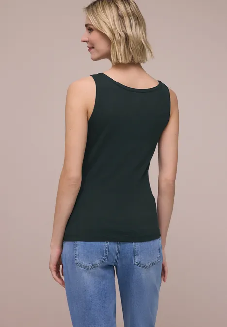 Basis top deep bound green Achteraanzicht van een vrouw in een zwart hemdje en blauwe spijkerbroek voor een effen achtergrond.