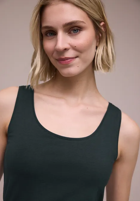 Basis top deep bound green Buste van een vrouw in een mouwloos, zwart topje tegen een neutrale achtergrond.