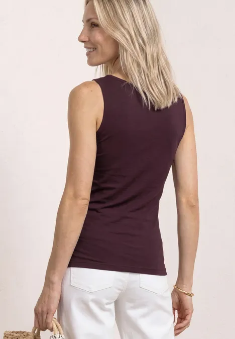 Vrouw van achteren met blond haar, bordeaux top en witte broek.