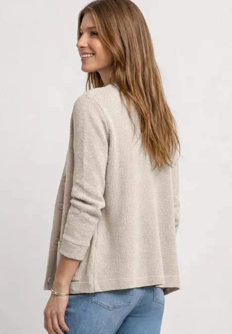 Vrouw van achteren in een beige cardigan en spijkerbroek tegen neutrale achtergrond.