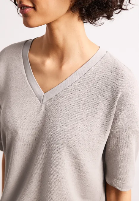 Vrouw met krullend haar draagt lichtgrijs V-hals shirt met korte mouwen.