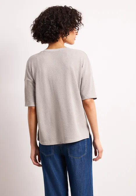 Achteraanzicht van een persoon met krullend haar in een lichtgrijs T-shirt en blauwe spijkerbroek voor witte achtergrond