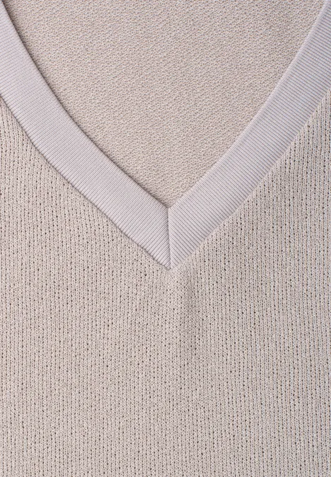 Close-up van een beige gebreide trui met V-hals.