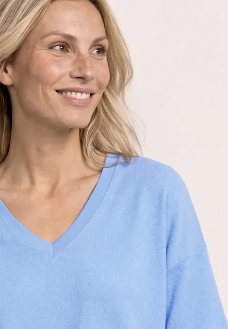 Vrouw met blond haar in een lichtblauw V-hals shirt tegen een lichte achtergrond.