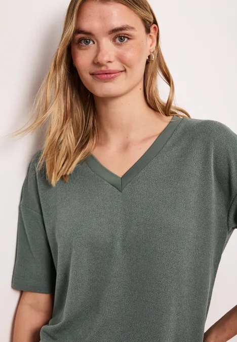 Vrouw in kaki V-hals T-shirt met korte mouwen voor een lichte achtergrond.