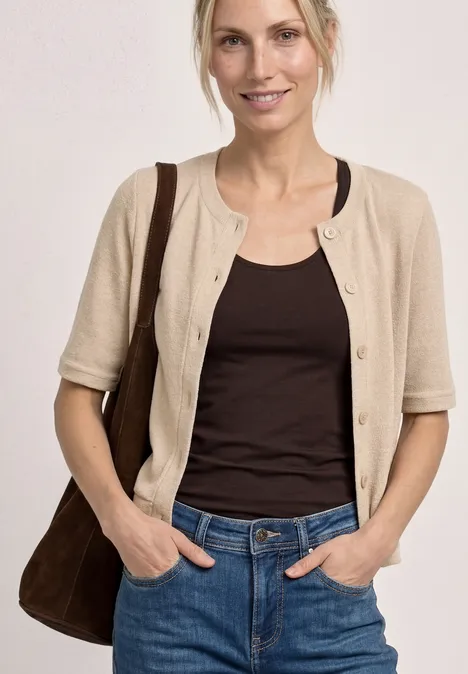 Vrouw borst tot heup, draagt beige cardigan, bruin topje, spijkerbroek en bruine schoudertas.