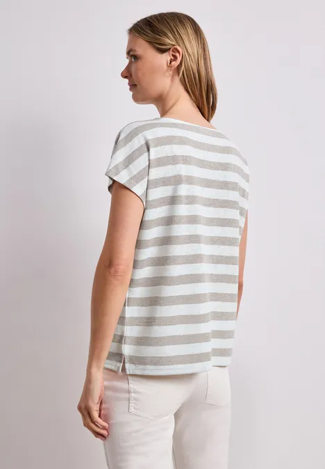 Shirt met hangende schouders, strepen en glitter timeless beige Vrouw van opzij met de rug naar de camera, draagt een grijs-wit gestreept T-shirt en een lichte broek.