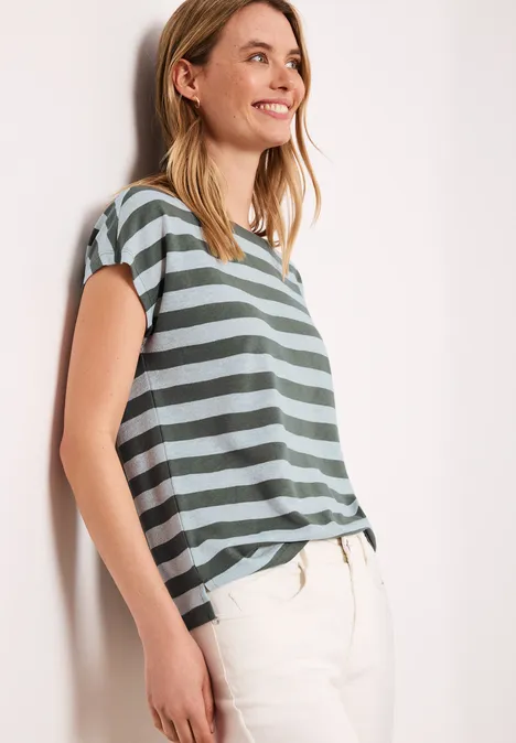 Shirt met hangende schouders, strepen en glitter bound green Een vrouw leunt tegen een muur, draagt een groen-grijs gestreept T-shirt met korte mouwen en een lichte broek.