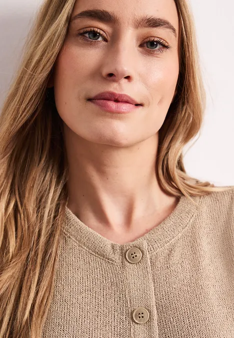 Gebreid gilet met glitter timeless beige Een persoon met lang haar draagt een beige gebreide trui met knopen.