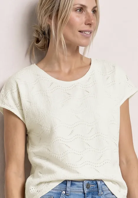 Vrouw met een wit, kortgebreid shirt met golvend patroon, gecombineerd met een spijkerbroek.