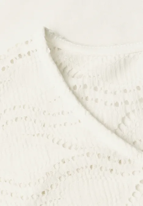 Close-up van een crèmekleurig gehaakt topje met V-hals en golvend patroon.