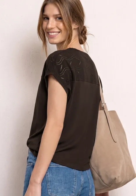 Vrouw in een zwart topje met kant, blauwe jeans en een grote beige tas over de schouder, zijaanzicht.