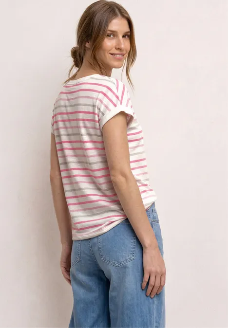 Frau steht seitlich, trägt gestreiftes T-Shirt und blaue Jeans vor neutralem Hintergrund.