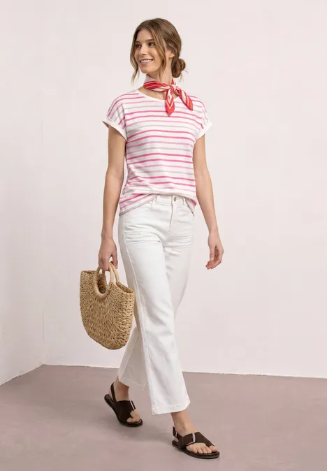 Frau im gestreiften T-Shirt, weißer Hose, rotem Halstuch, Strohtasche und schwarzen Sandalen.