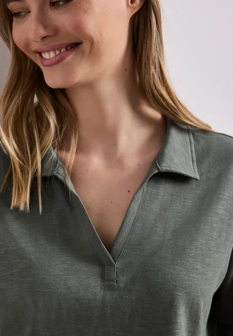 Iemand met lang haar draagt een groen poloshirt met een open kraag.