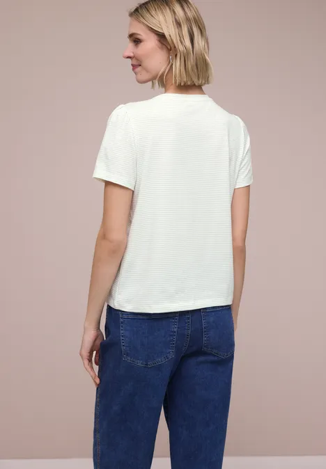 Rugaanzicht van een persoon met een wit t-shirt en blauwe jeans tegen een neutrale achtergrond.