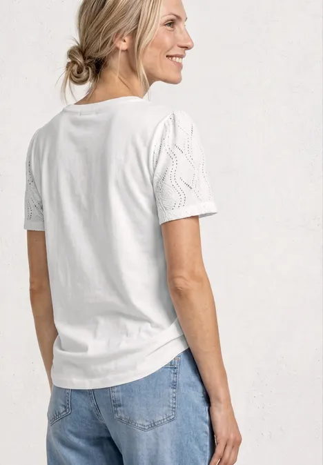 Vrouw zijwaarts met wit T-shirt met gestructureerde mouwen, haar losjes in een knot.