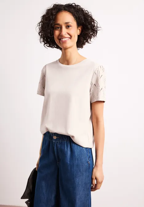 Shirt met ronde hals en kanten mouwen clay sand Vrouw in wit t-shirt met kanten mouwen en blauwe jeans, houdt een zwarte jas in haar hand.