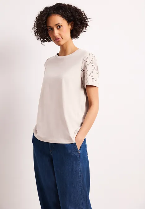 Shirt met ronde hals en kanten mouwen clay sand Vrouw in crèmekleurig T-shirt met kantmouwen en wijde blauwe jeans, handen in de zakken.