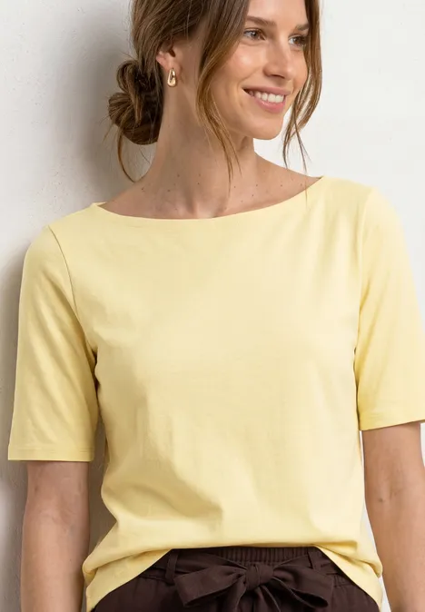 Basic T-Shirt mit U-Boot-Ausschnitt soft yellow Frau mit hochgestecktem Haar in hellgelbem, kurzärmeligem Oberteil vor hellem Hintergrund.