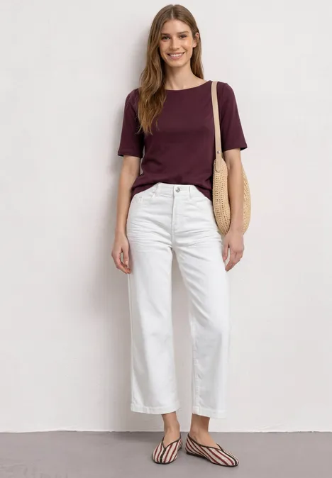 Basic T-Shirt mit U-Boot-Ausschnitt rustic rouge Frau trägt bordeauxrotes T-Shirt, weiße Hose, gestreifte Flip-Flops und Korbtasche.