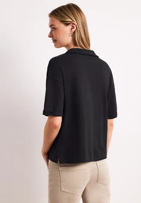 Een vrouw van achteren draagt een zwart poloshirt en een lichte broek.
