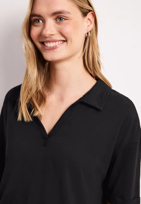 Glimlachende blonde vrouw in een zwart overhemd met V-hals en kraag voor een lichte achtergrond.