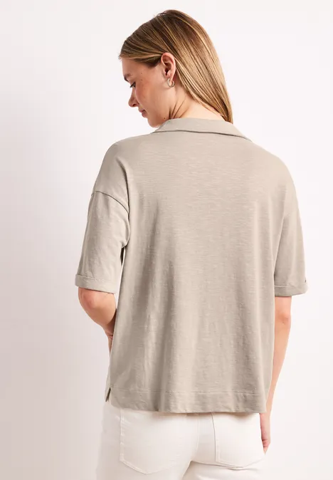 Vrouw van achteren in een beige T-shirt met korte mouwen en een witte spijkerbroek.