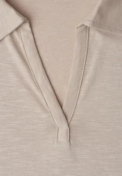 Close-up van een beige top met V-hals van lichtgewicht stof en zichtbare stiknaad.