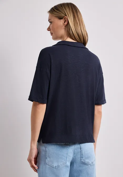 Achteraanzicht van een vrouw met blond haar, donkerblauw T-shirt en spijkerbroek.