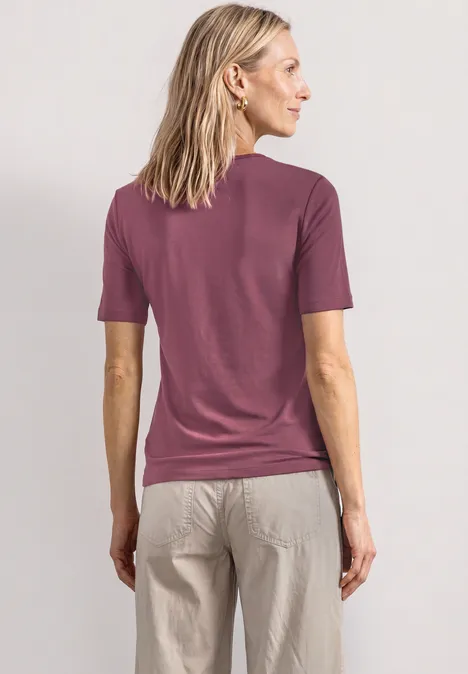 Basic T-Shirt mit Herzausschnitt dark clouded blush Rückansicht einer Frau in lila T-Shirt und beiger Hose.