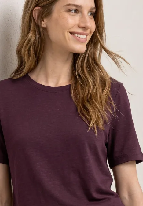 Vrouw met lang blond haar en eenvoudig paars T-shirt tot aan de taille.